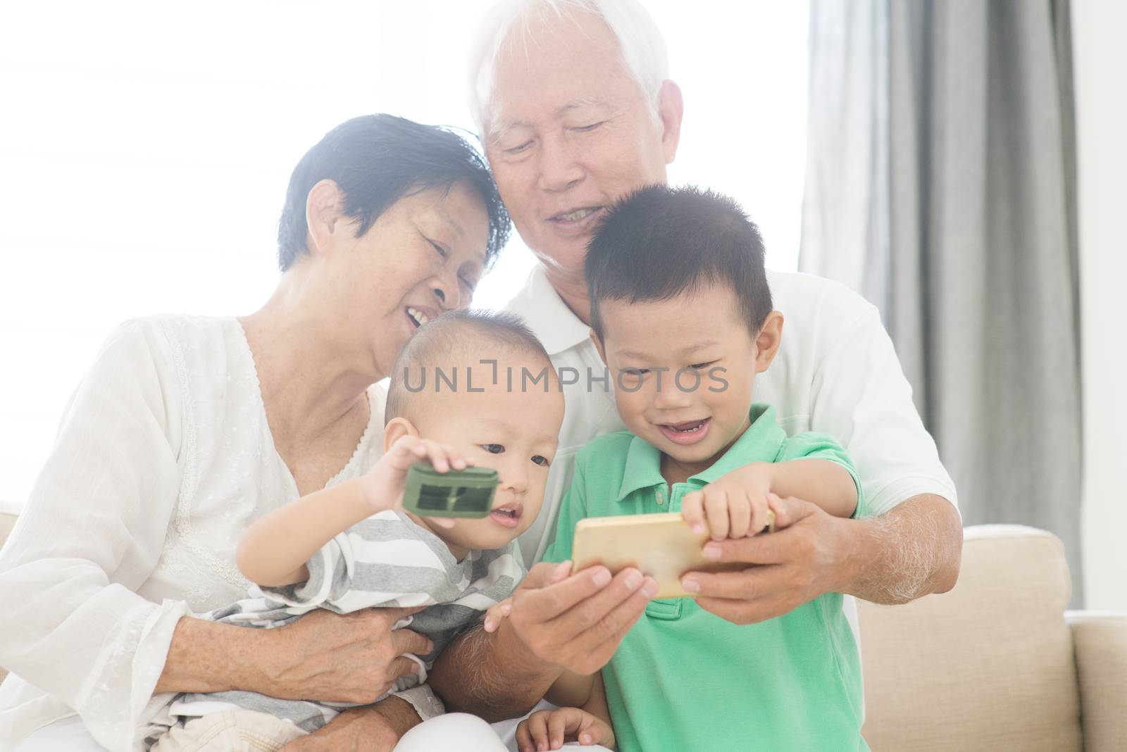 Portrait of happy Asian grandparents and grandchildren taking self photo using smart phone at home, family indoor lifestyle.