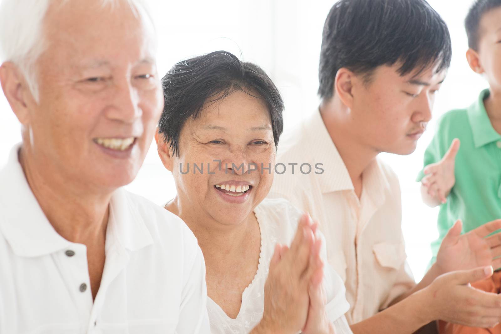 Candid of Asian family relaxed at home, clapping hands, multi generations people indoor lifestyle.