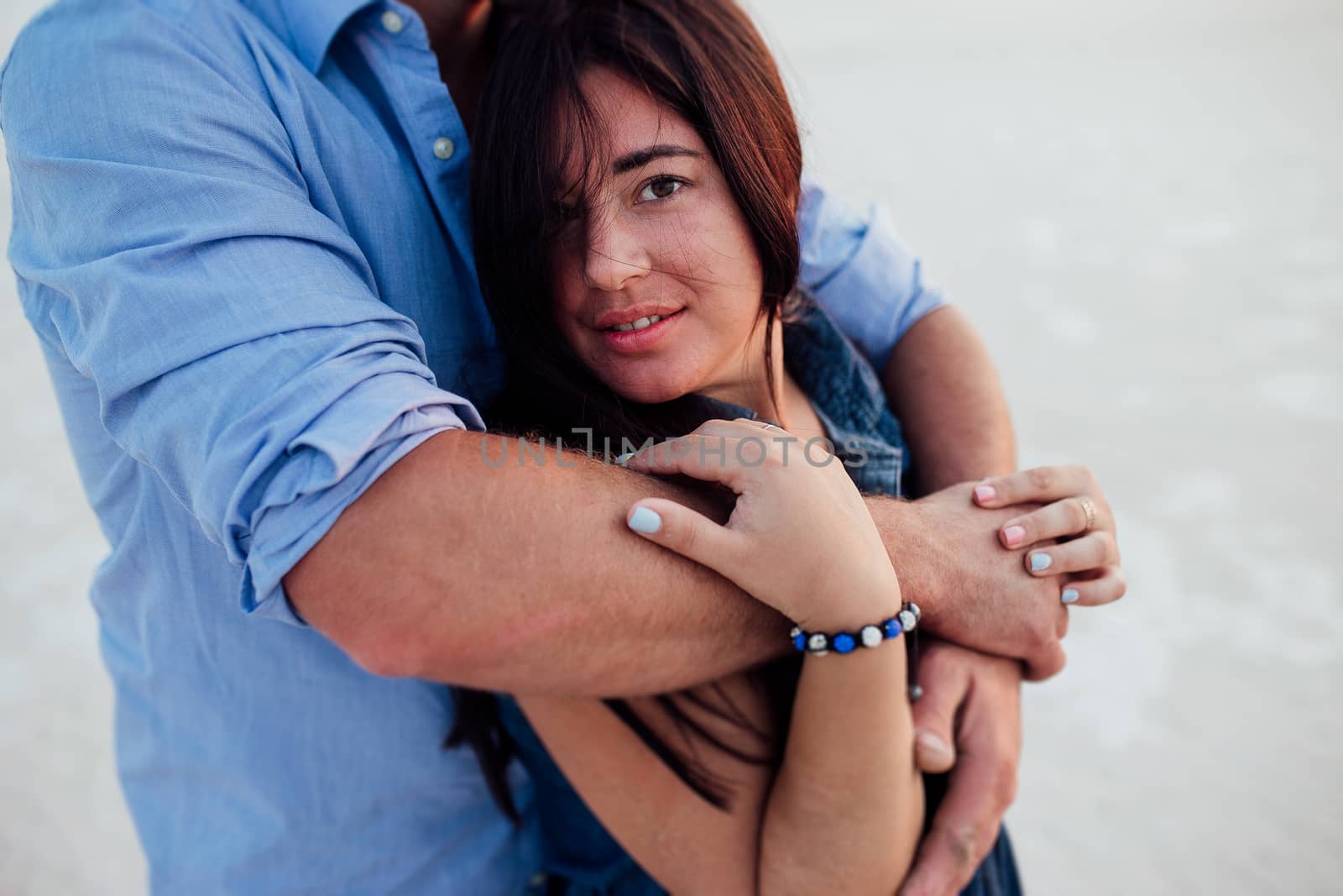 Young happy family walking along the seashore. Husband and wife walking on the beach. Husband holding his wife at the back and she is looking at the camera and smiling.