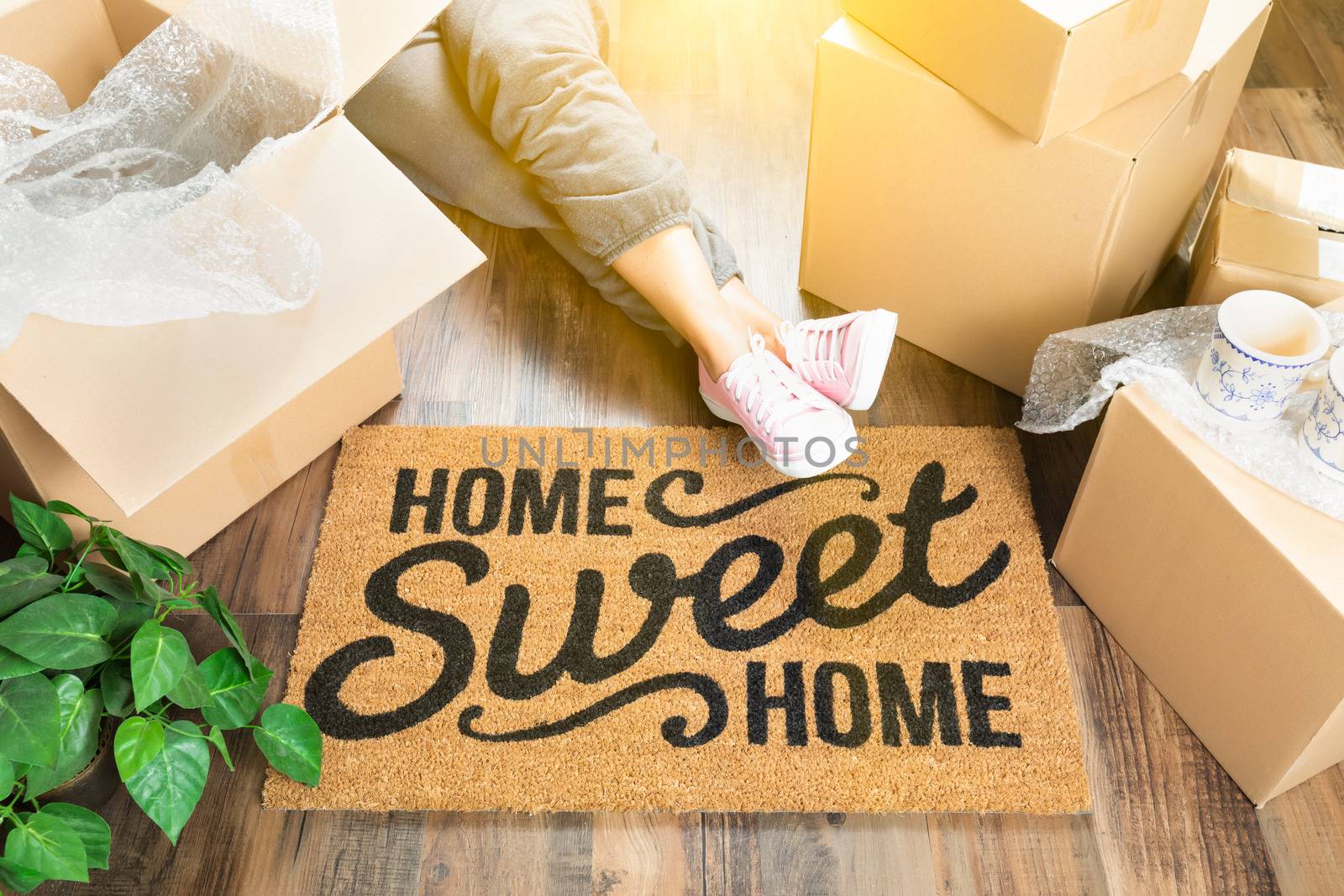 Woman Wearing Sweats Relaxing Near Home Sweet Home Welcome Mat, Moving Boxes and Plant.