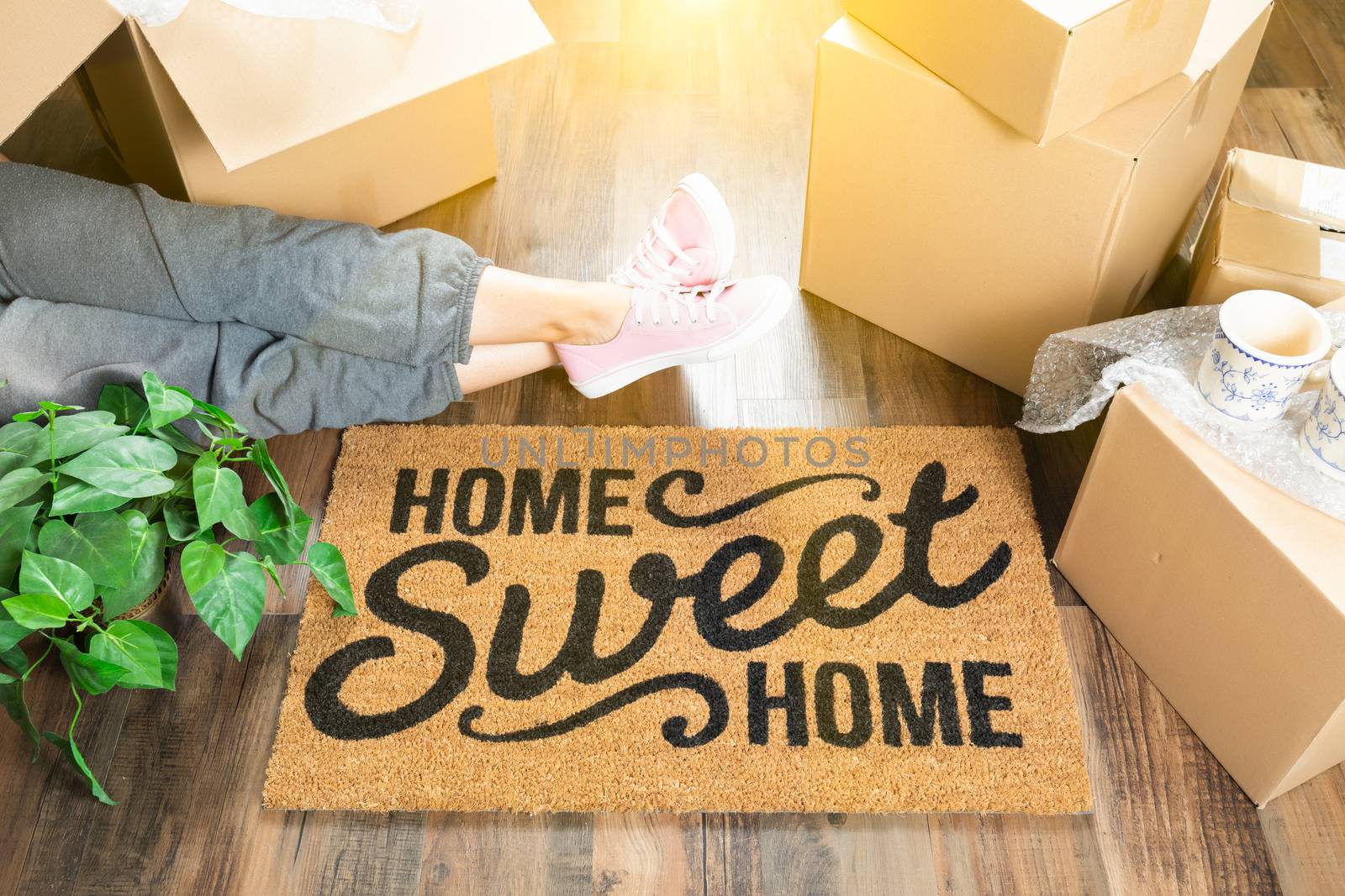 Woman Wearing Sweats Relaxing Near Home Sweet Home Welcome Mat, Moving Boxes and Plant.