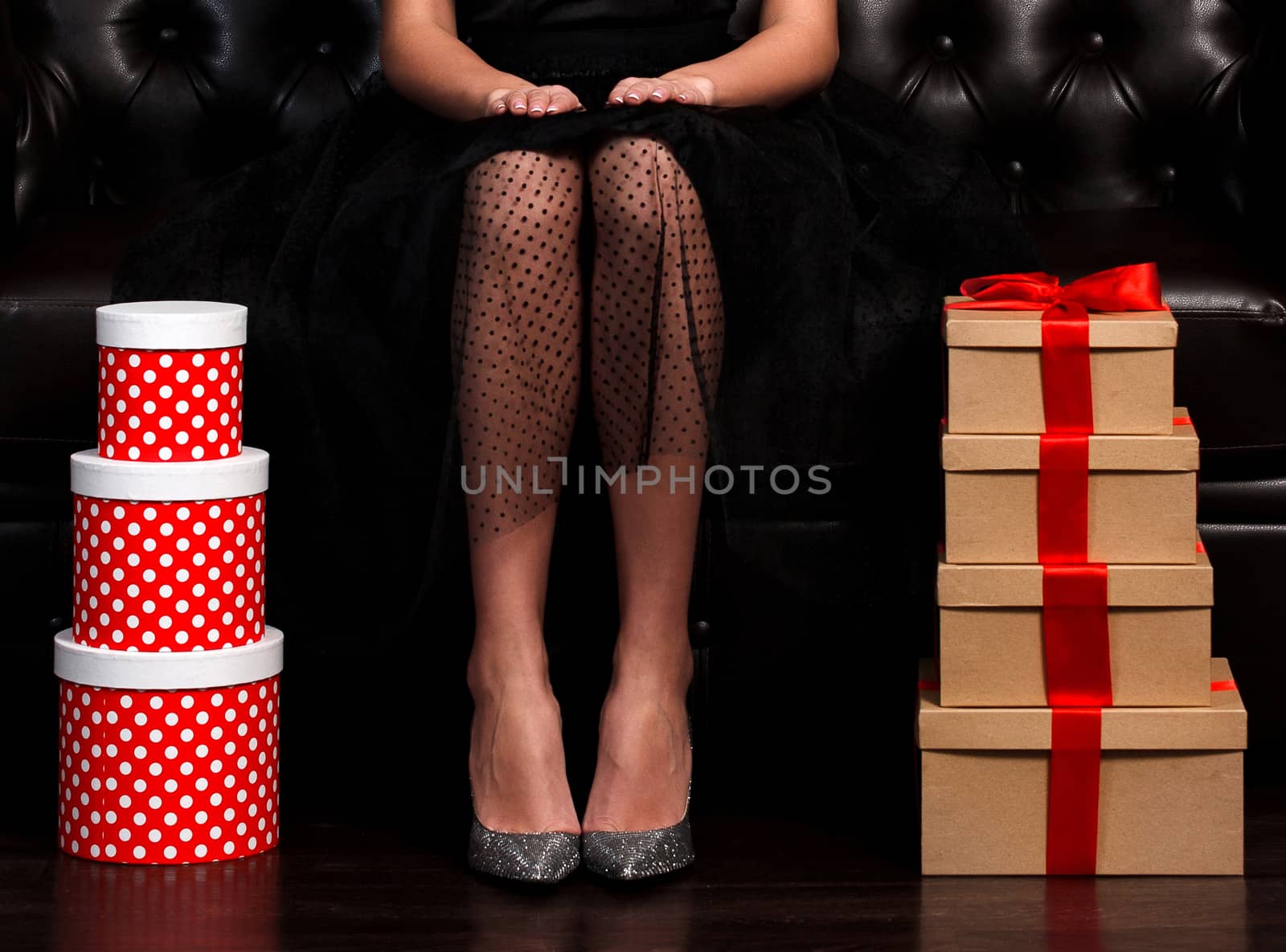 Pretty woman sittin on leather sofa between stacks of presents