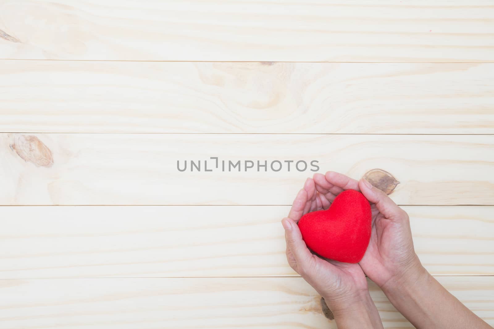 Hand holding a red heart on wooden table with copy space for valentine day concept.