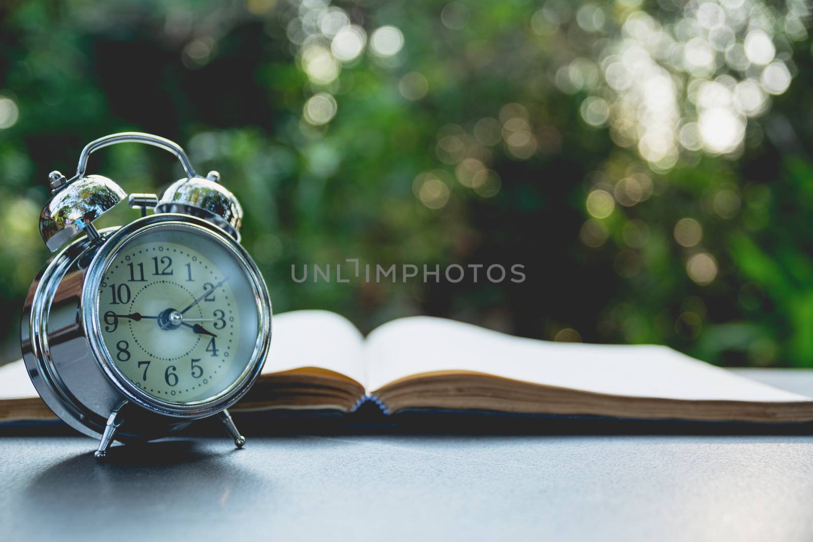 Open book with alarm clock. Book open on old wooden table on nature background.