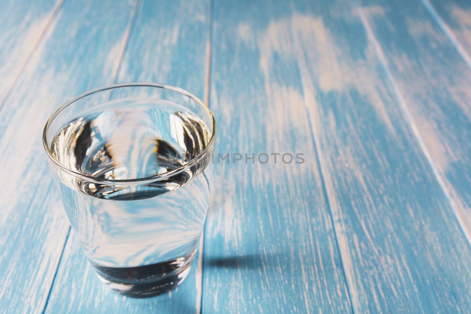 Water in glass on blue and wooden table background.