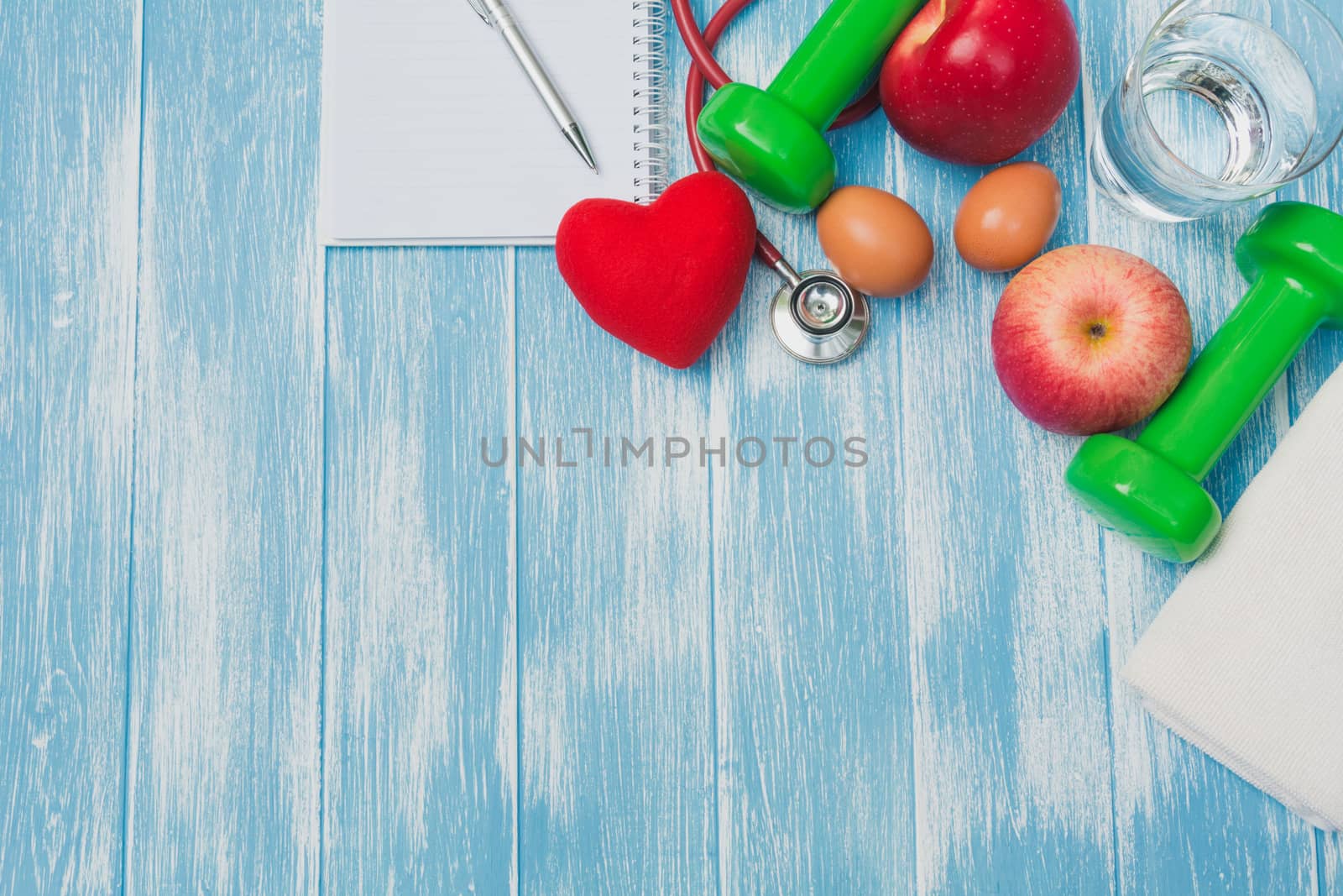 Top view of sportswear, sports equipment, dumbbells and stethoscope on blue and wooden table.
