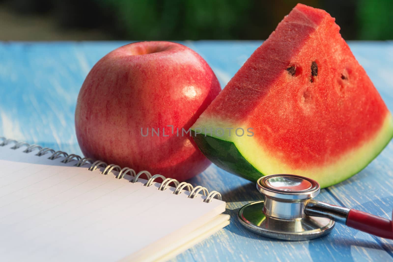 Stethoscope, apple, watermelon and note on blue and wooden table for health concept.
