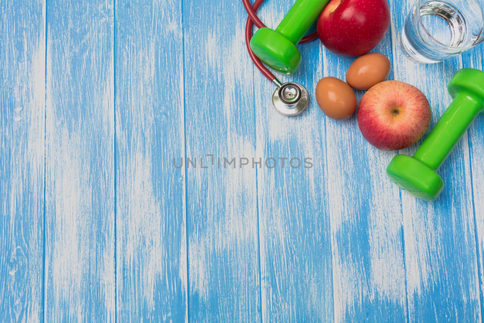 Top view of sportswear, sports equipment, dumbbells and stethoscope on blue and wooden table.