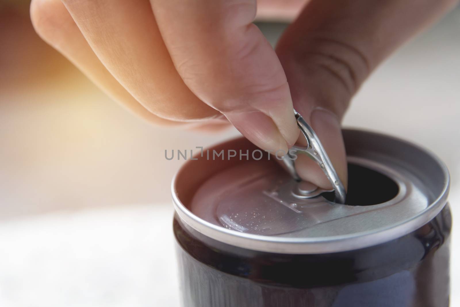 Hand opening an iron can. Can with a drink of cola.