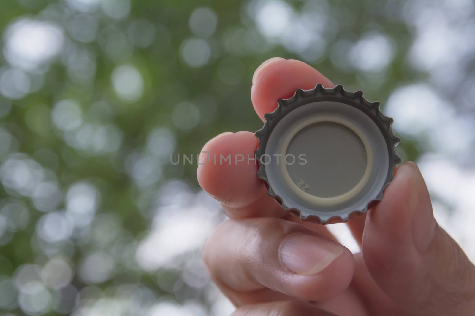 Hand holding a bottle caps on nature background.