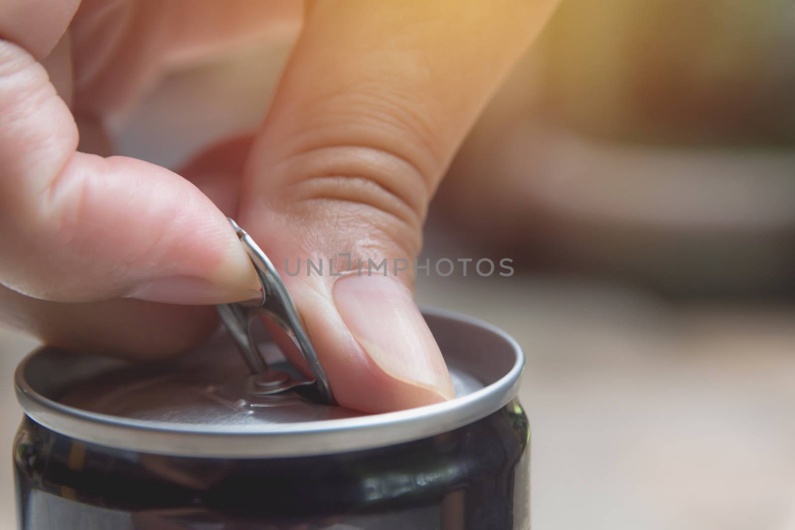 Hand opening an iron can. Can with a drink of cola.