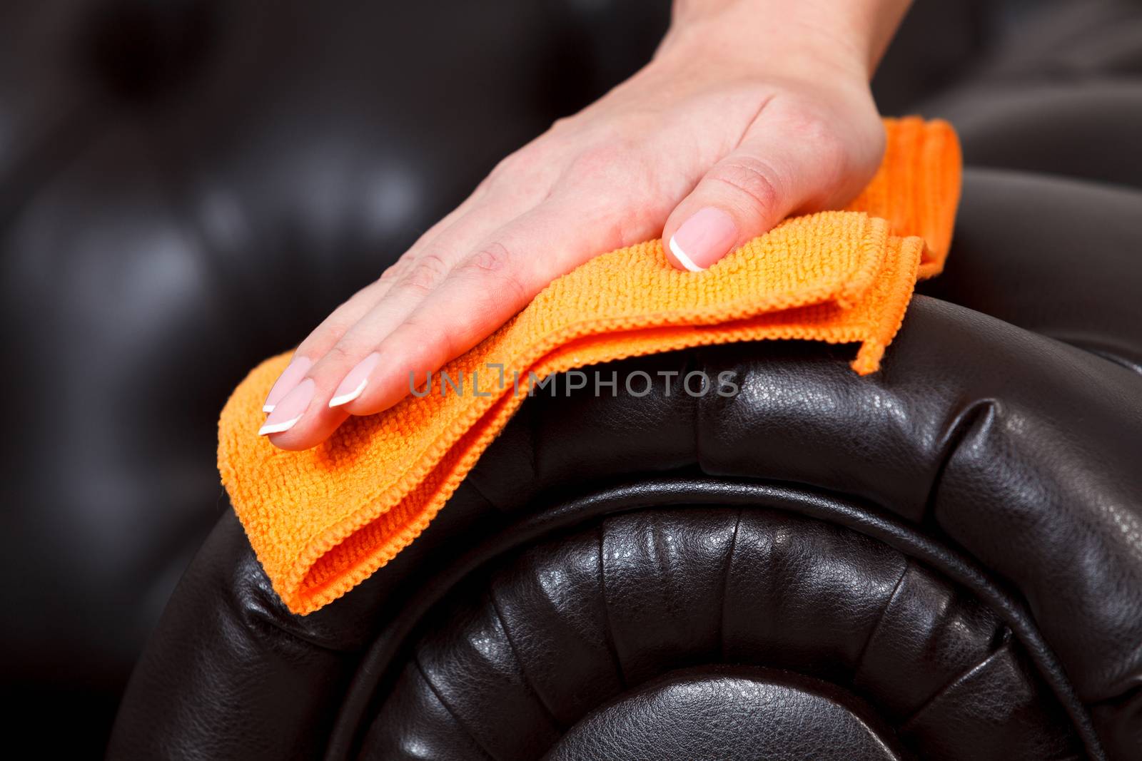 Closeup shot of female hand with beautiful manicured fingers wiping brown leather couch