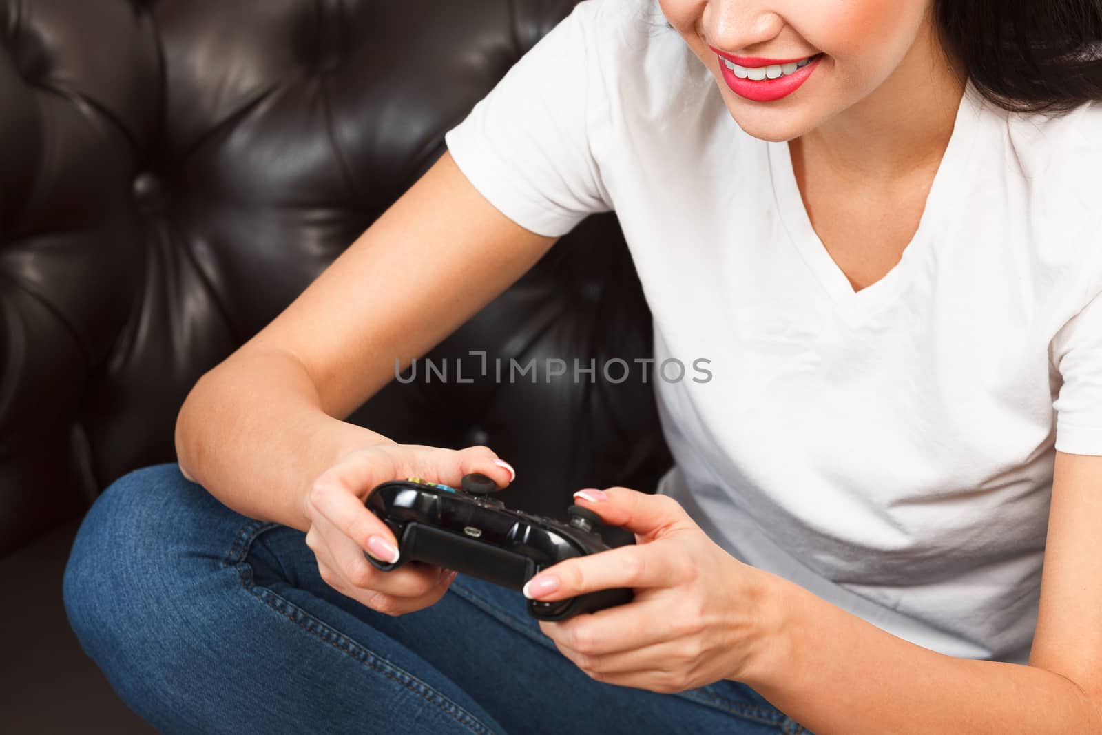 Woman gamer sitting on brown leather sofa and playing a video ga by Nobilior