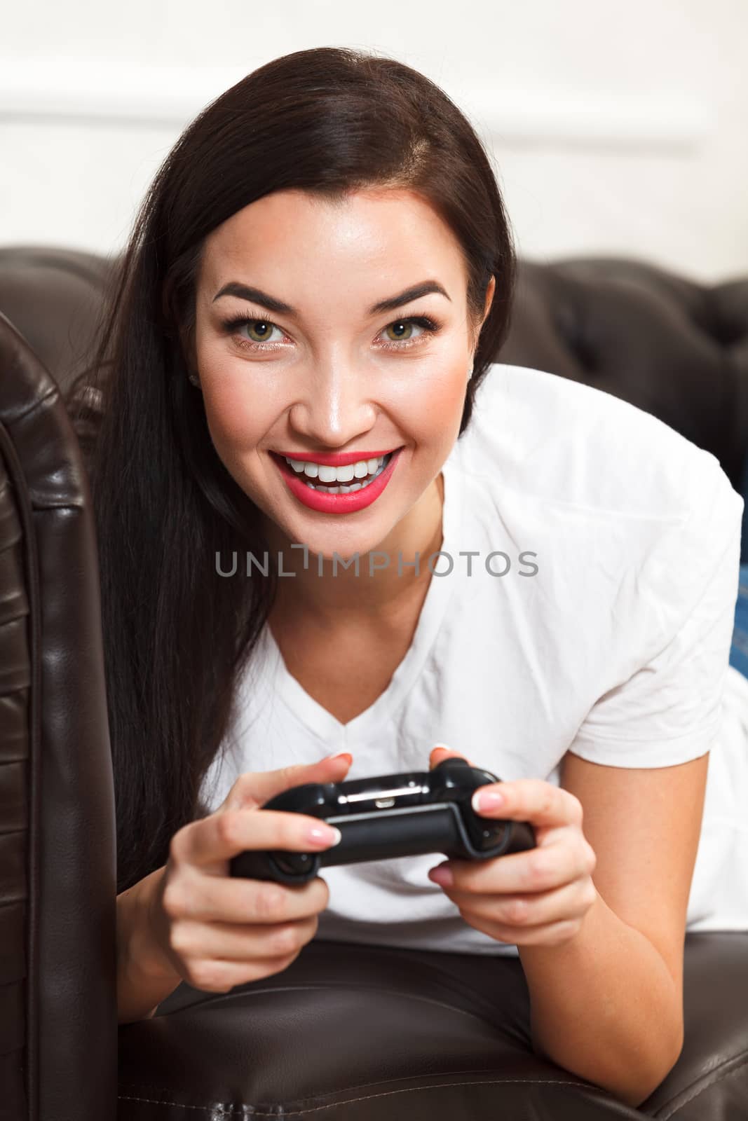 Woman gamer lies on brown leather sofa and plays a video game by Nobilior