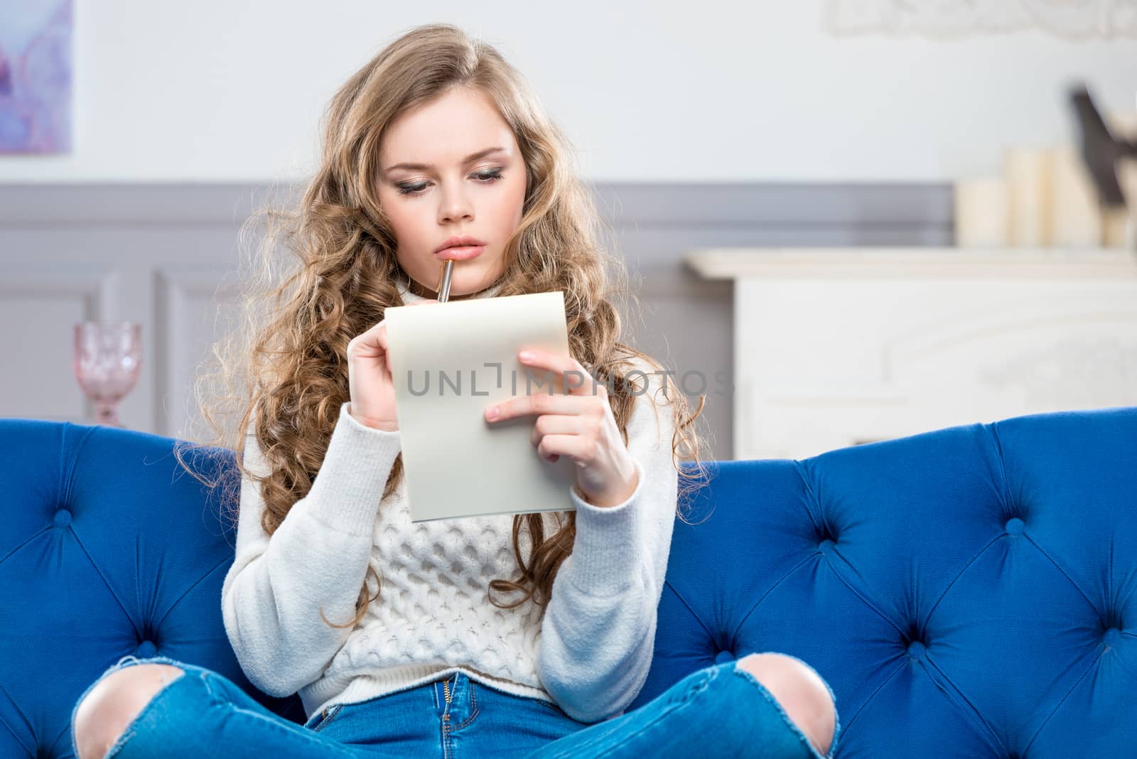 portrait of a pensive young girl with a sheet of paper sitting on the couch