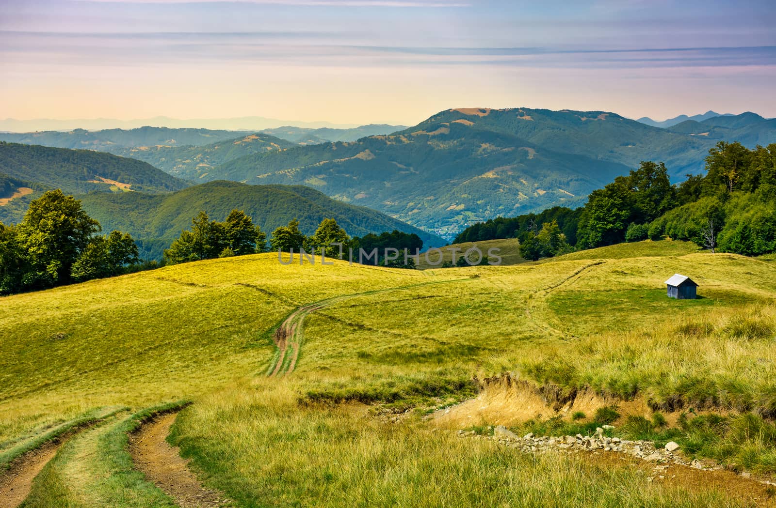 truck path down the grassy hill. wooden shed on the hillside. beautiful landscape with Krasna mountain ridge in the distance in evening light. Carpathian mountains, Ukraine