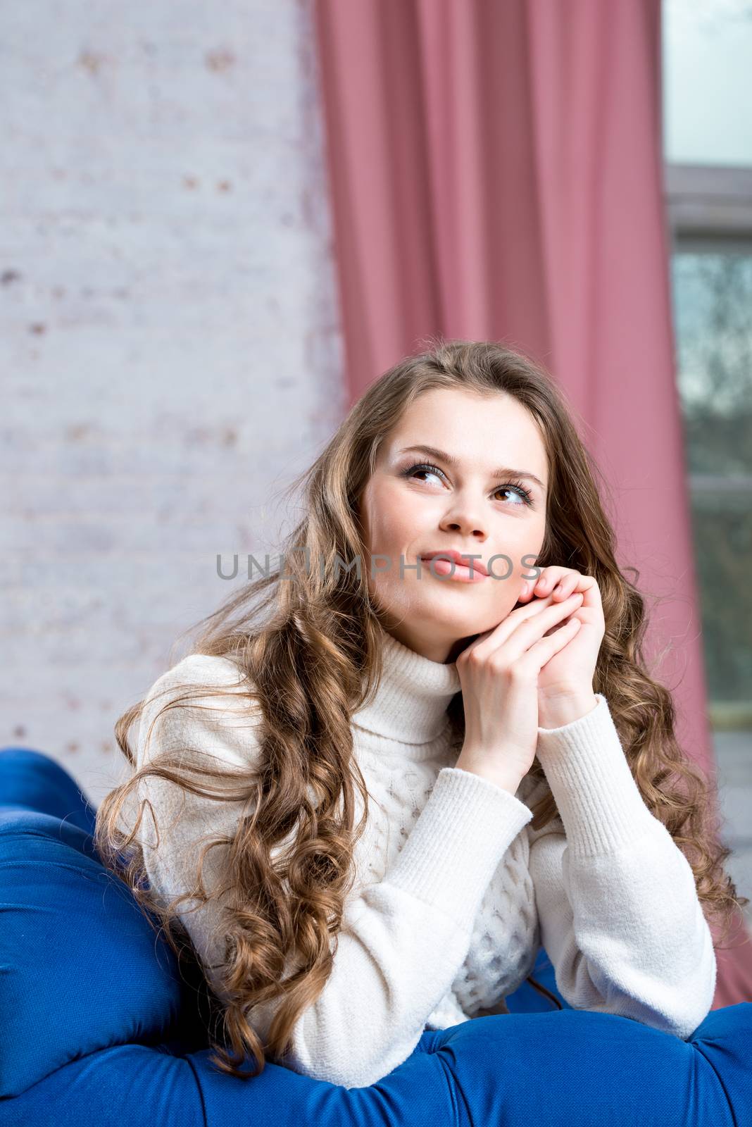 portrait of a young beautiful woman in a white knitted sweater on a blue sofa
