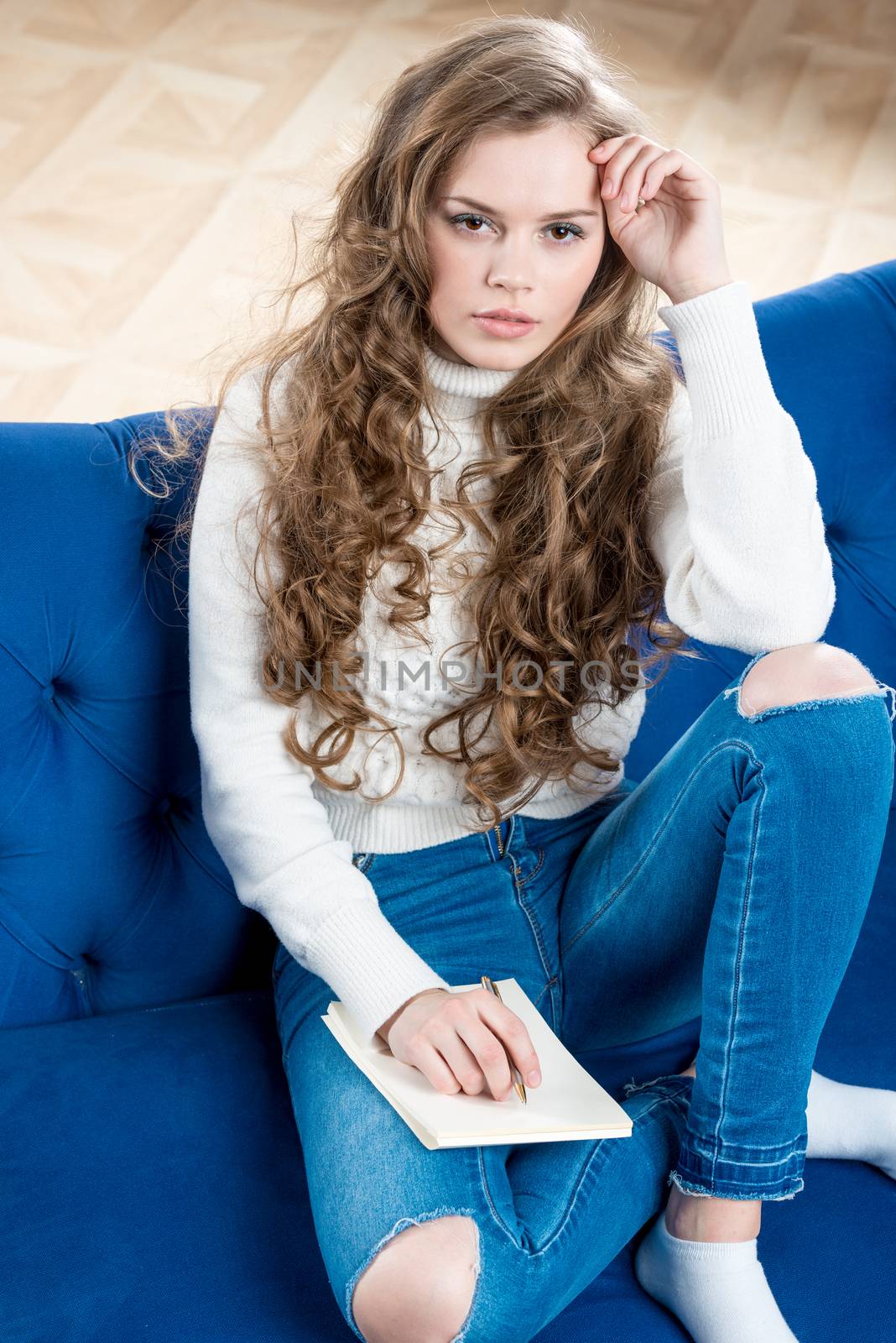 Shot of a beautiful woman in a sweater and jeans on the couch with a notebook