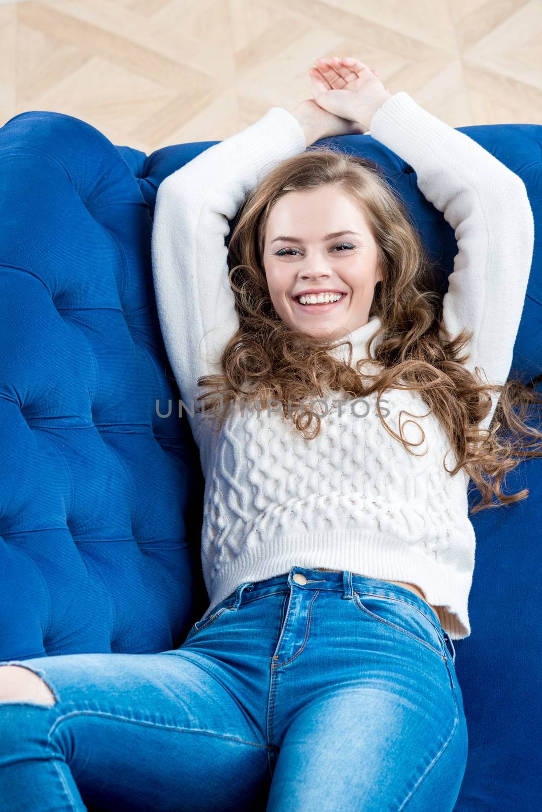 happy slim model in a sweater and jeans relaxes on the couch by kosmsos111