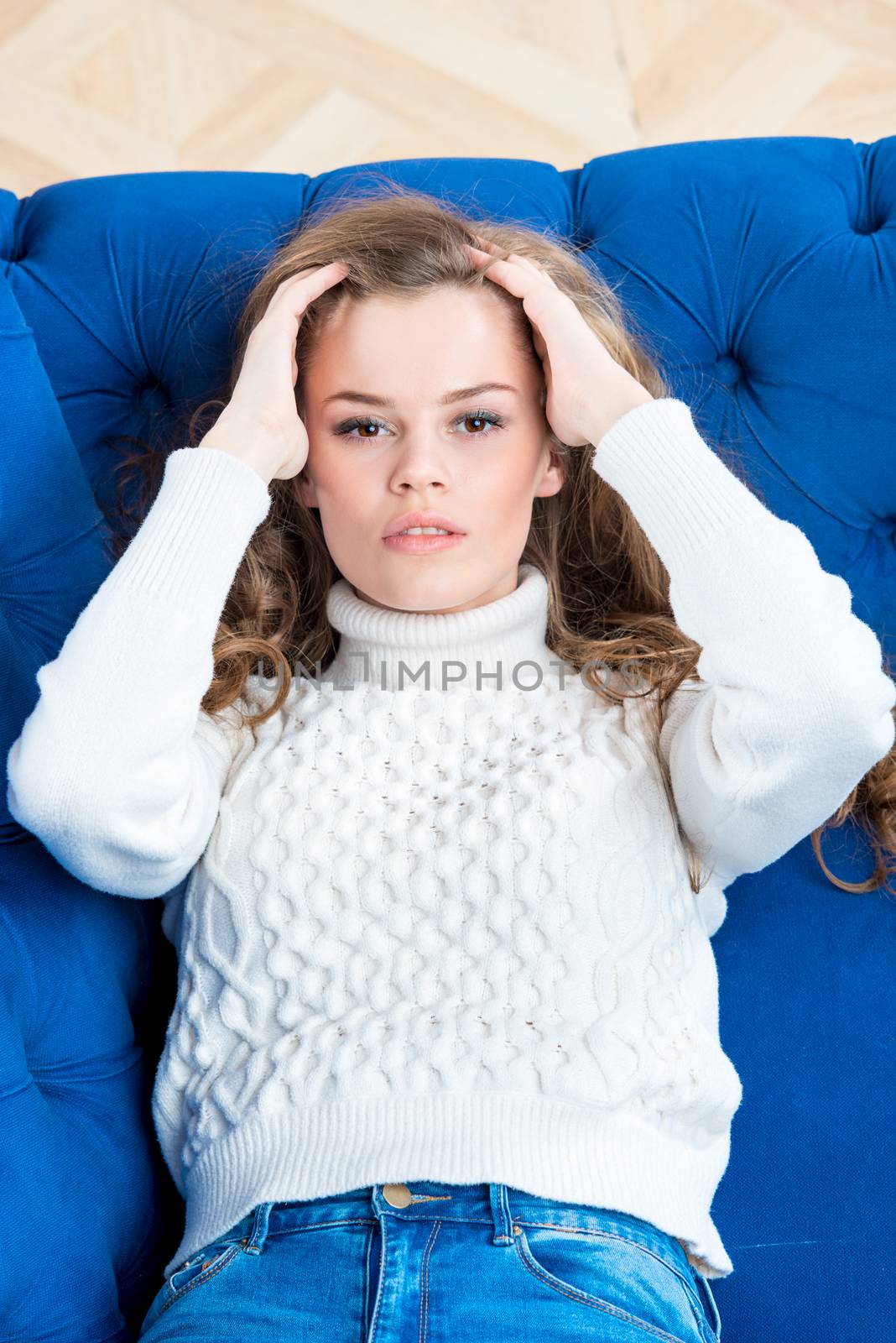 vertical portrait of a beautiful girl posing on the sofa in the living room in a sweater