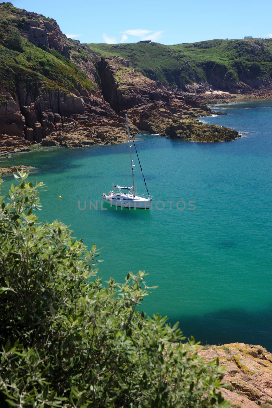 A sailboat at anchor in Portelet bay, Jersey, UK. Turquoise water and sunshine. Vertical format