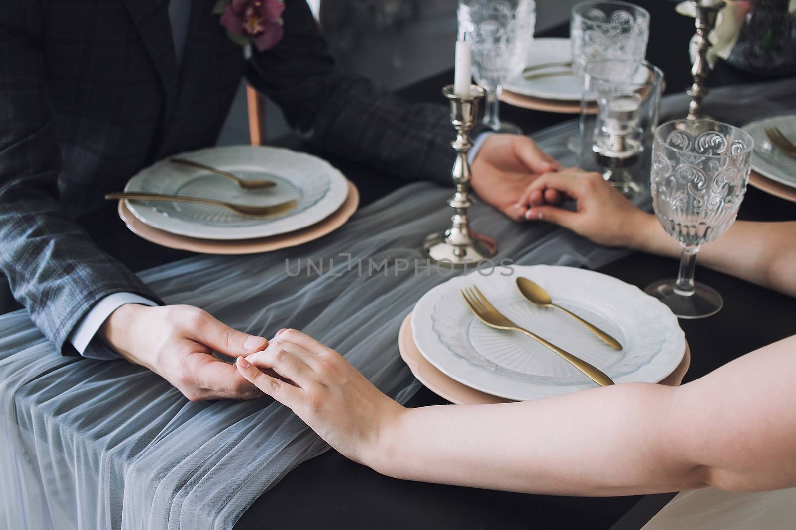 Closeup of couple hands on restaurant table with two glasses of champagne. Romantic couple holding each other's hand at dinner in a luxury restaurant. by 3KStudio