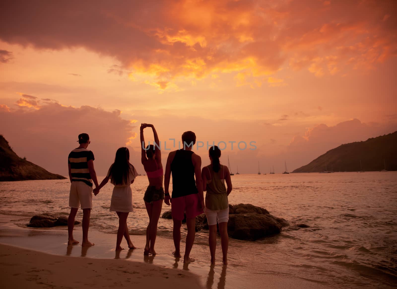 Group of happy people at sea beach at sunset