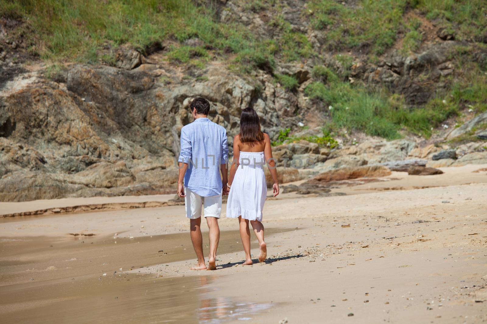 Happy couple walking on sand of tropical beach