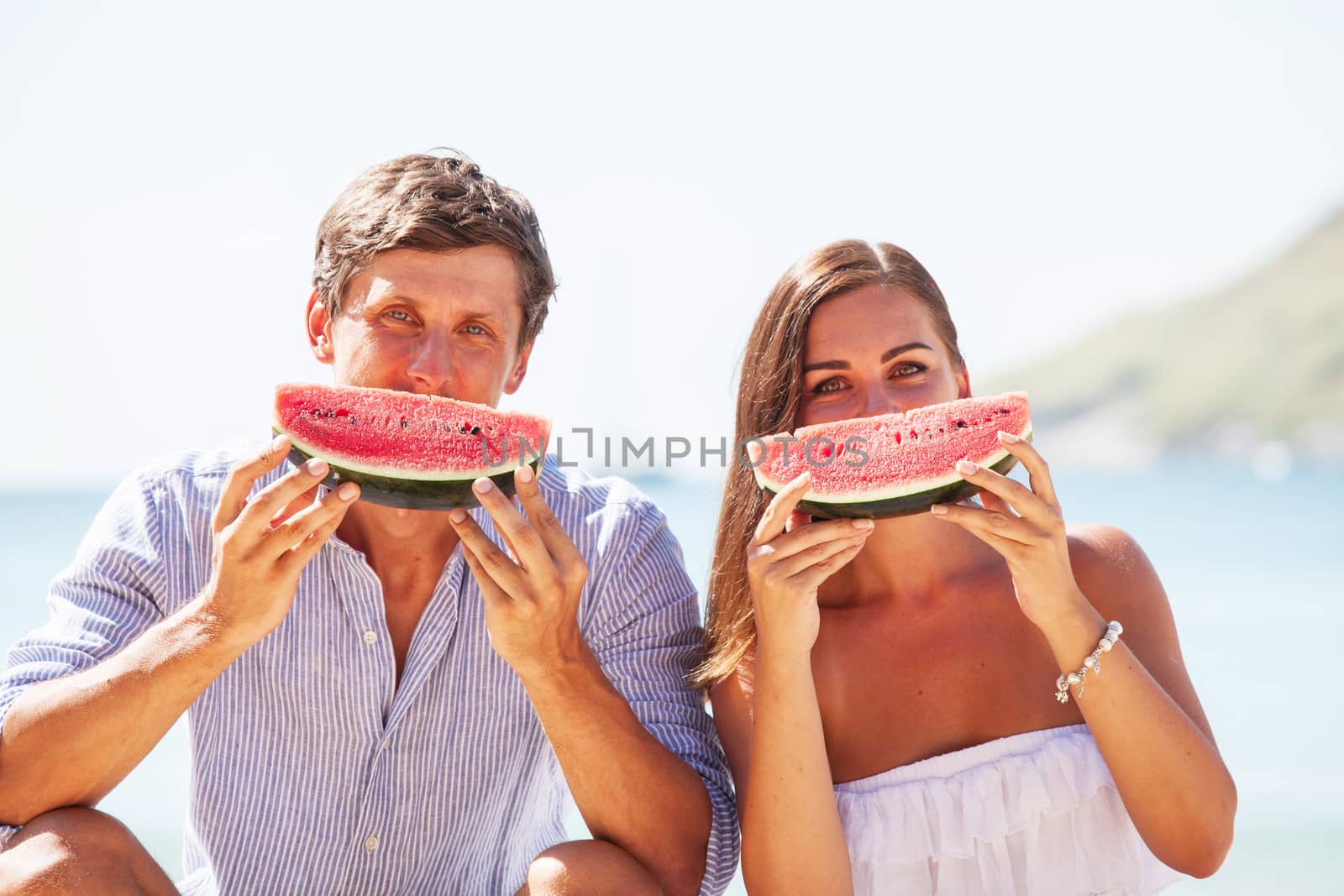 Cheerful couple eating watermelon at sea beach