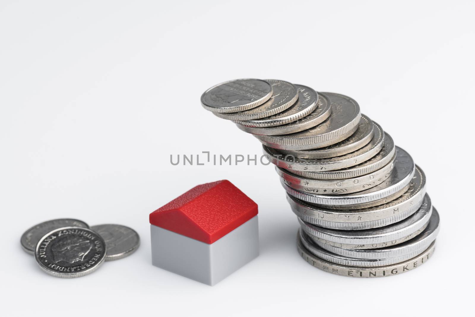 Conceptual visualization of property related financial act by means of coins with plastic miniature cottage for a white background
