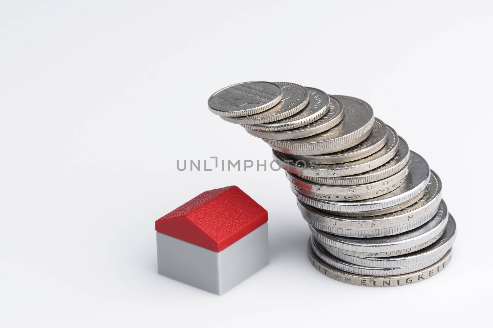 Conceptual visualization of property related financial act by means of coins with plastic miniature cottage for a white background
