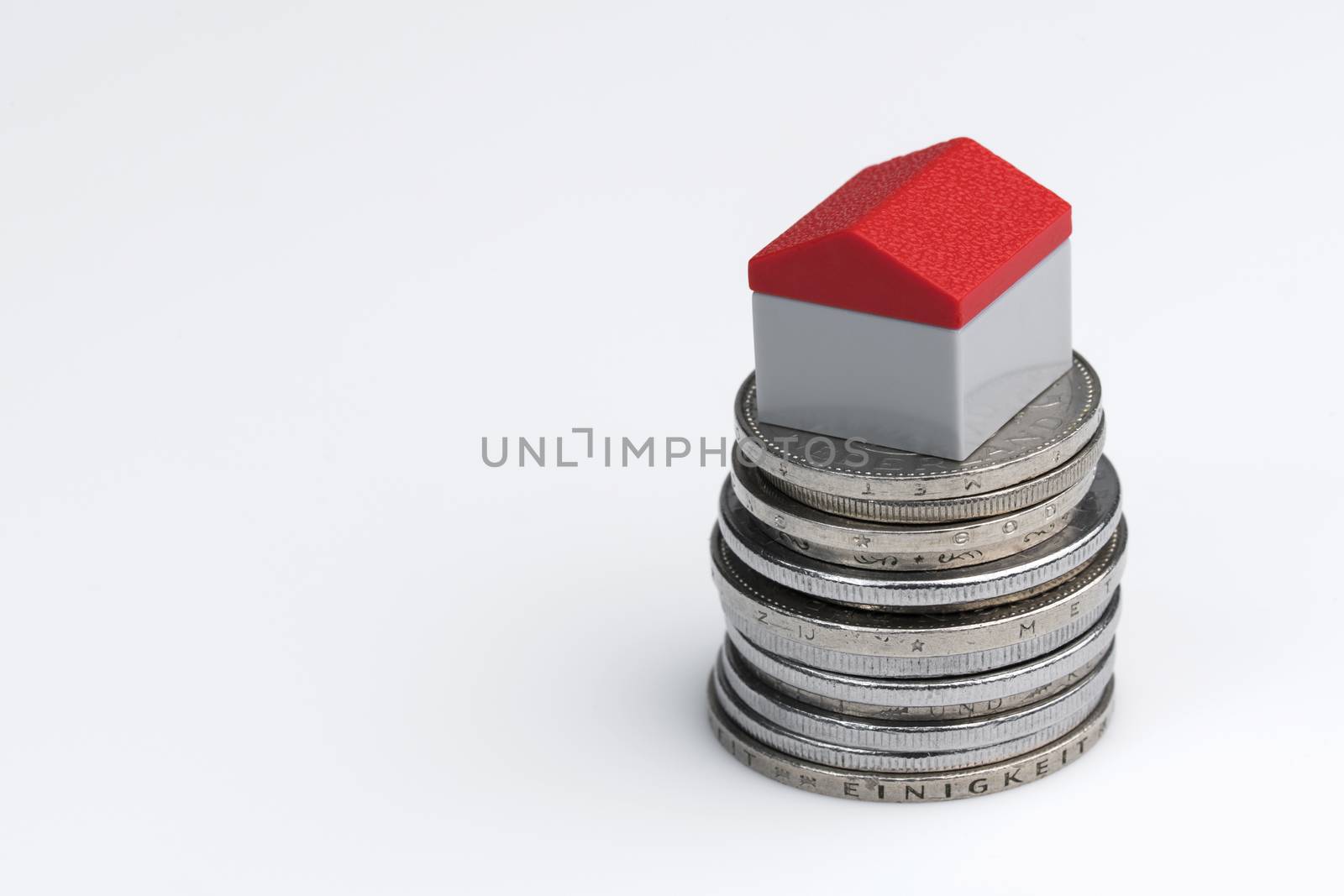 Conceptual visualization of property related financial act by means of coins with plastic miniature cottage for a white background
