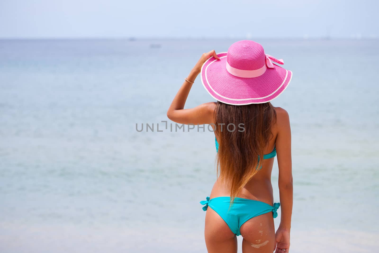 Woman in big hat standing on beach by the sea