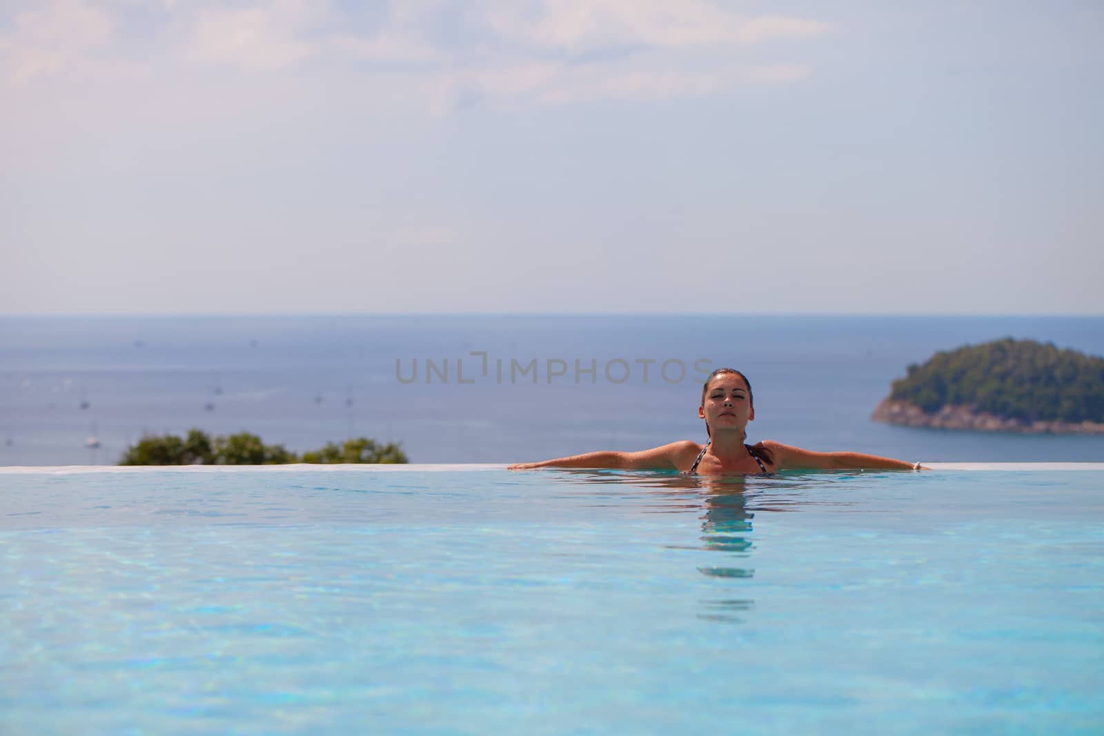 Girl resting at the end of a stunning infinity pool. Sea on background