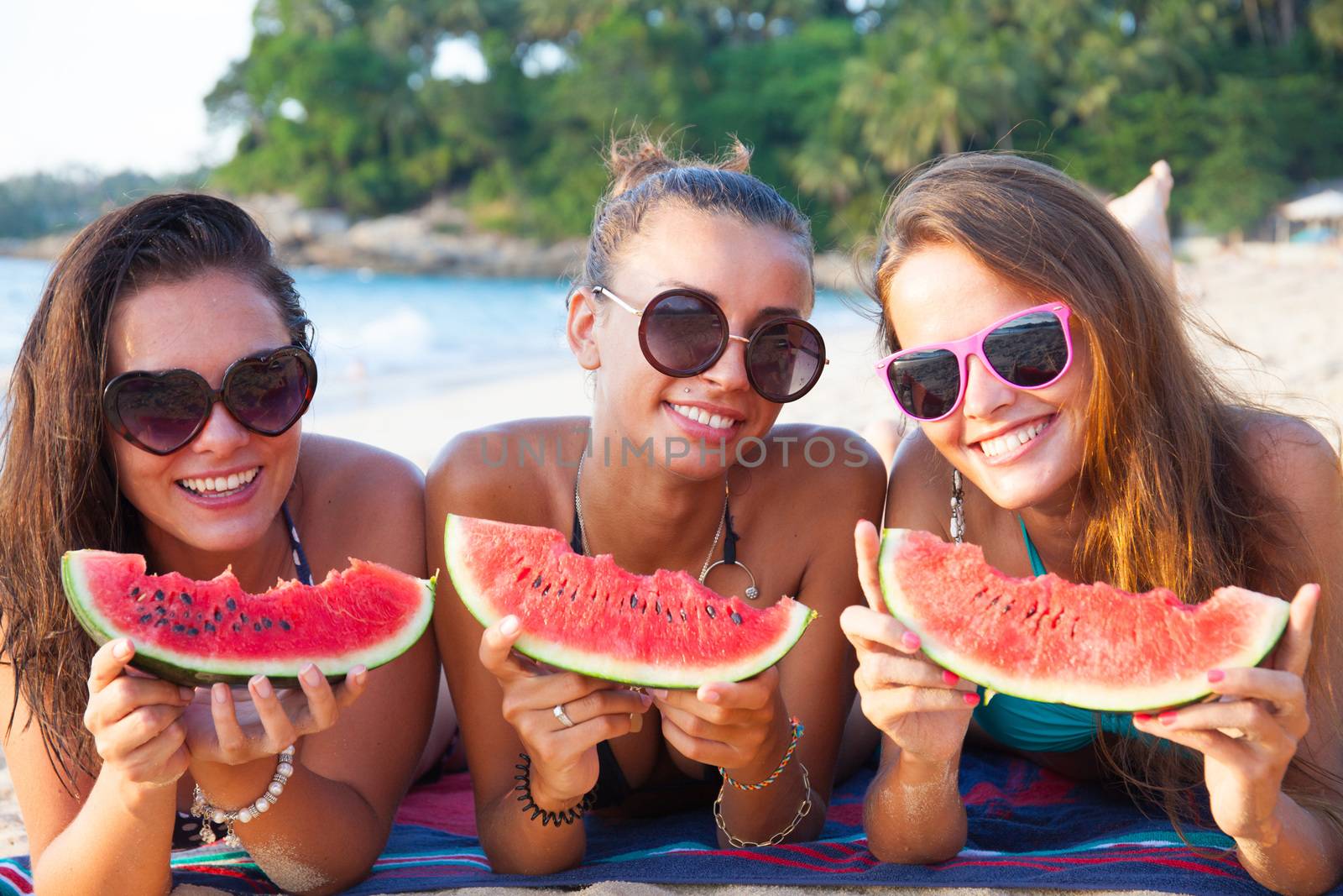 Happy smiling female friends eating watermelon on beach