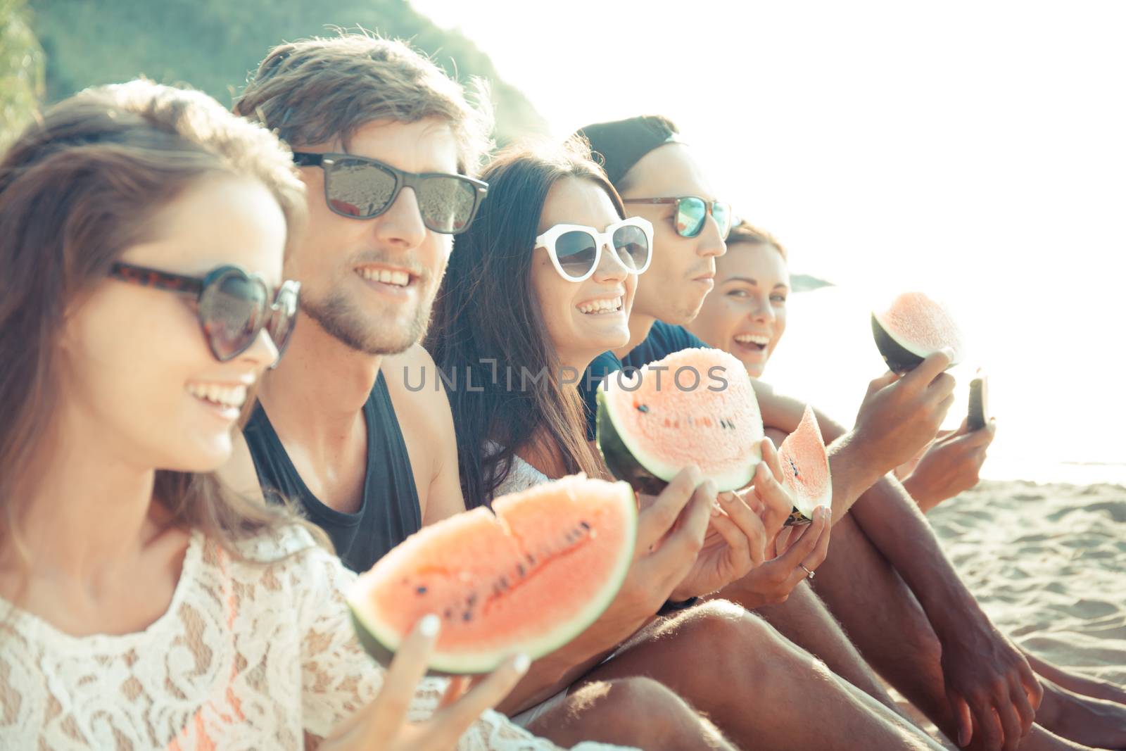 Happy young friends eating watermelon on beach
