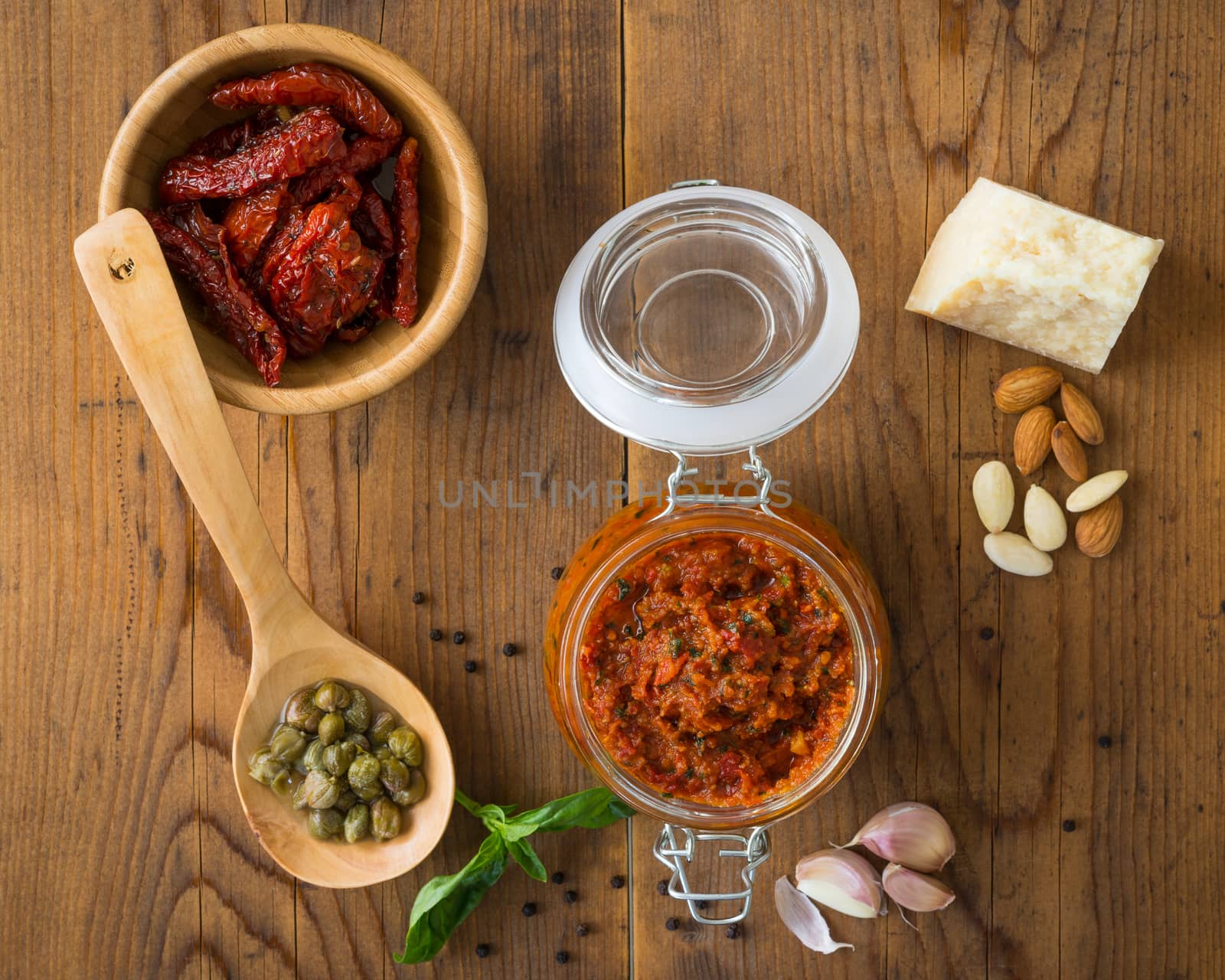 Pesto with dry tomatoes and almonds in a glass jar on a wooden table