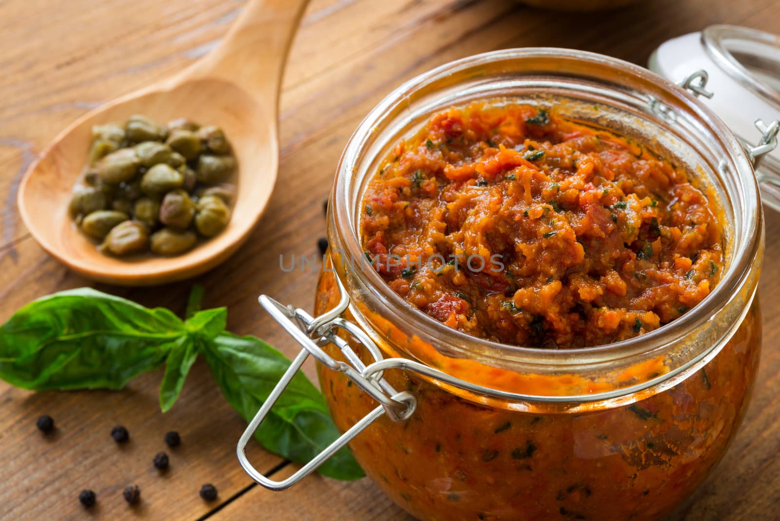 Pesto with dry tomatoes and almonds in a glass jar on a wooden table