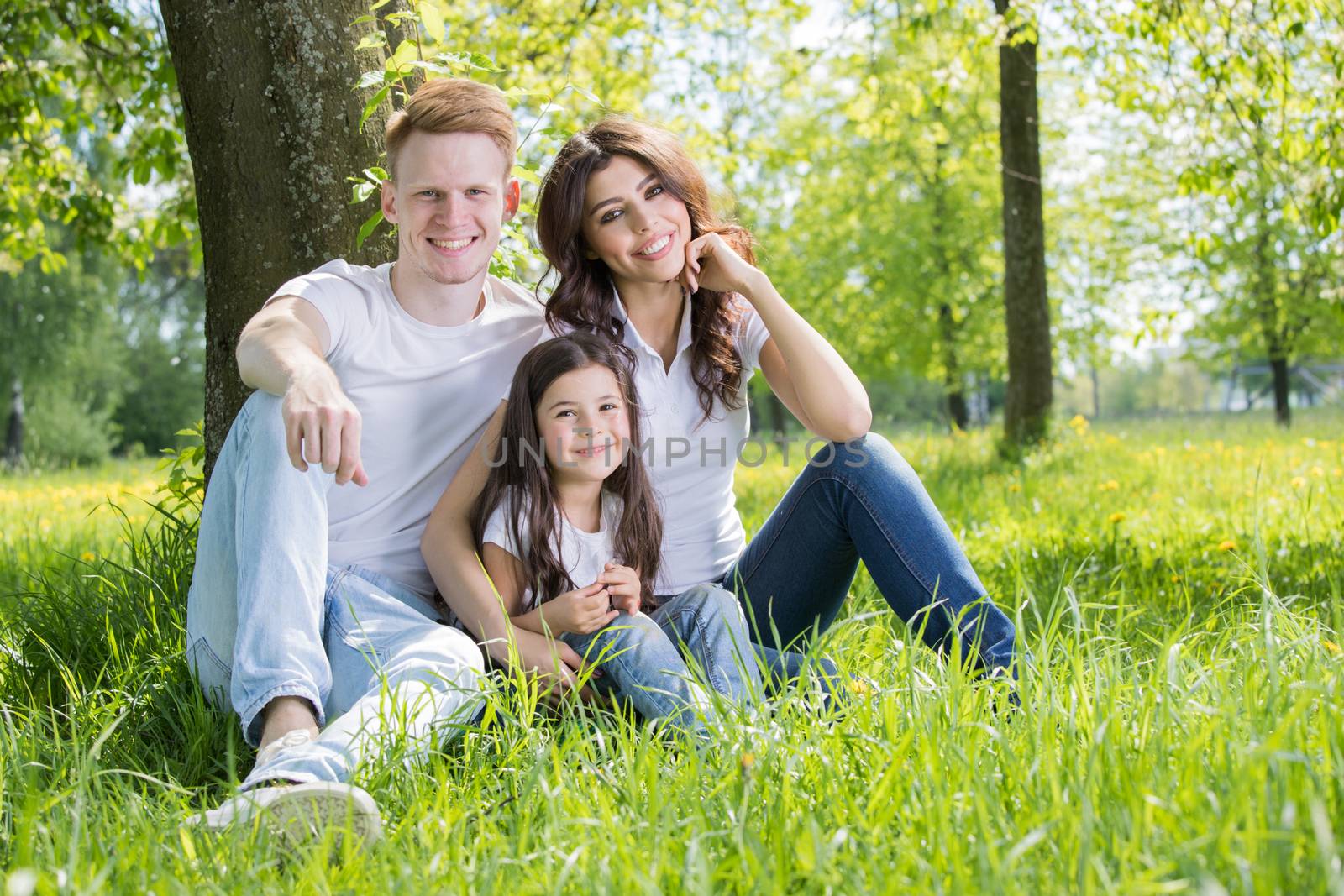 Happy family with man, woman and child leaning on tree in city park
