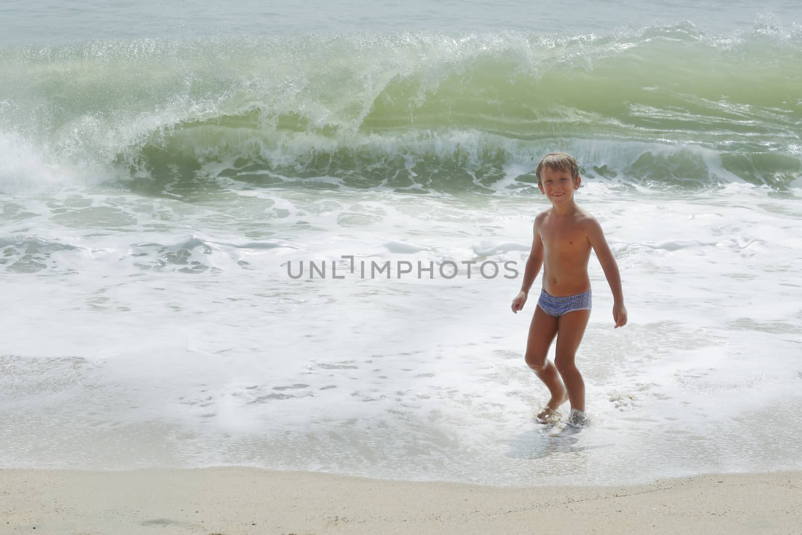 Happy child playing in sea waves. Kid having fun outdoors. Summer vacation and healthy lifestyle concept