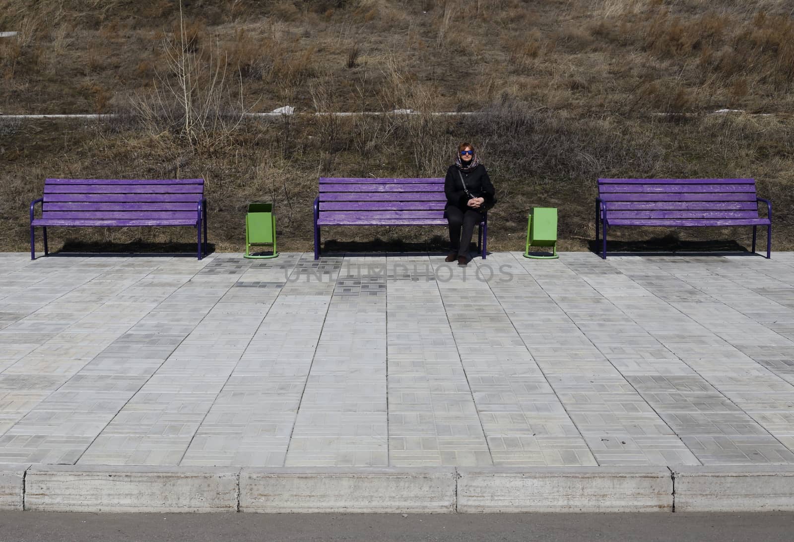 young woman sitting on a bench. next few benches. on the street early spring. on the ground paving stones.