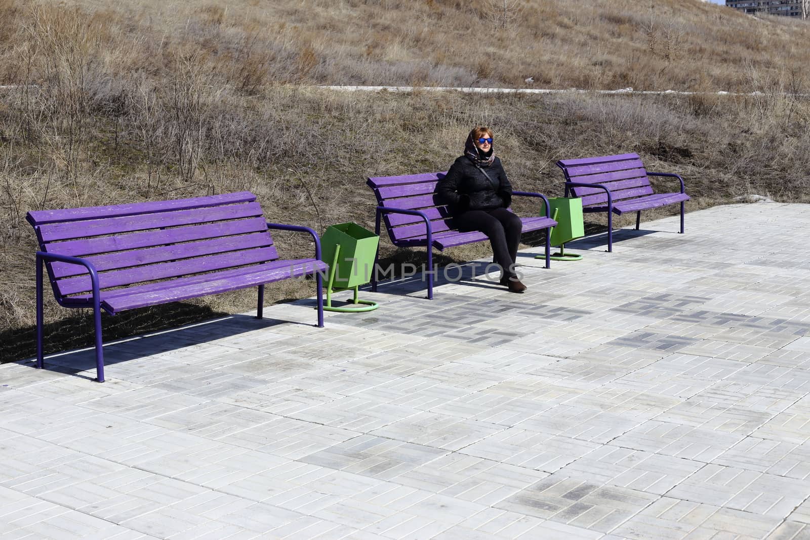 young woman sitting on a bench. next few benches. on the street early spring. on the ground paving stones.