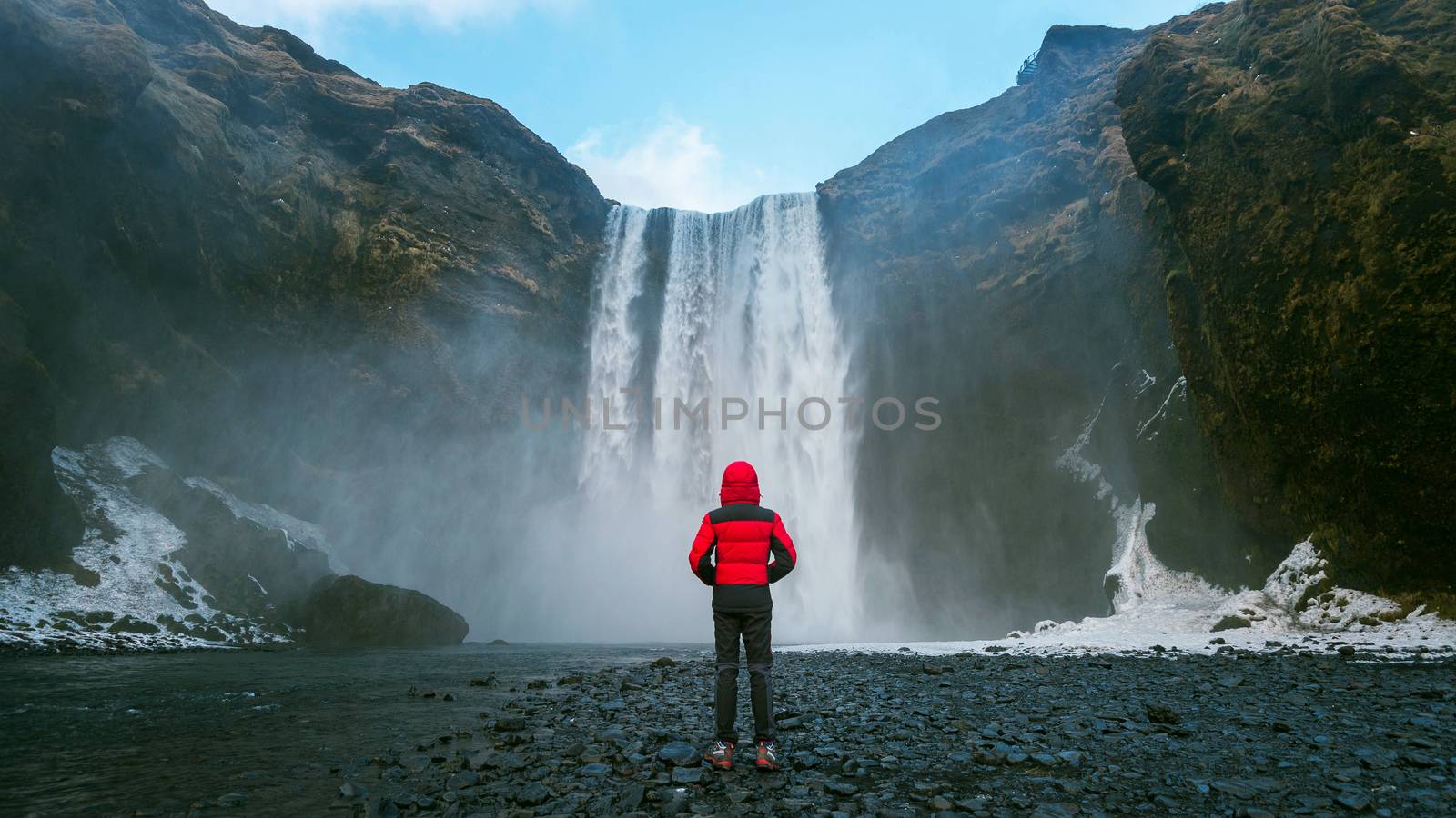 Skogafoss waterfall in Iceland. Guy in red jacket looks at Skoga by gutarphotoghaphy