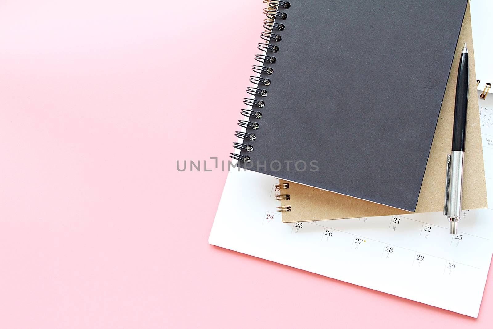 Top view or flat lay of notebooks, calendar and pen on pink background by sureeporn