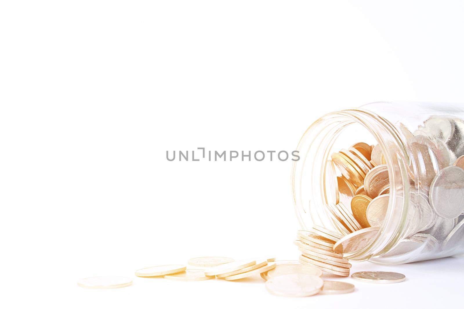 Coins scattered from glass jar on white background by sureeporn
