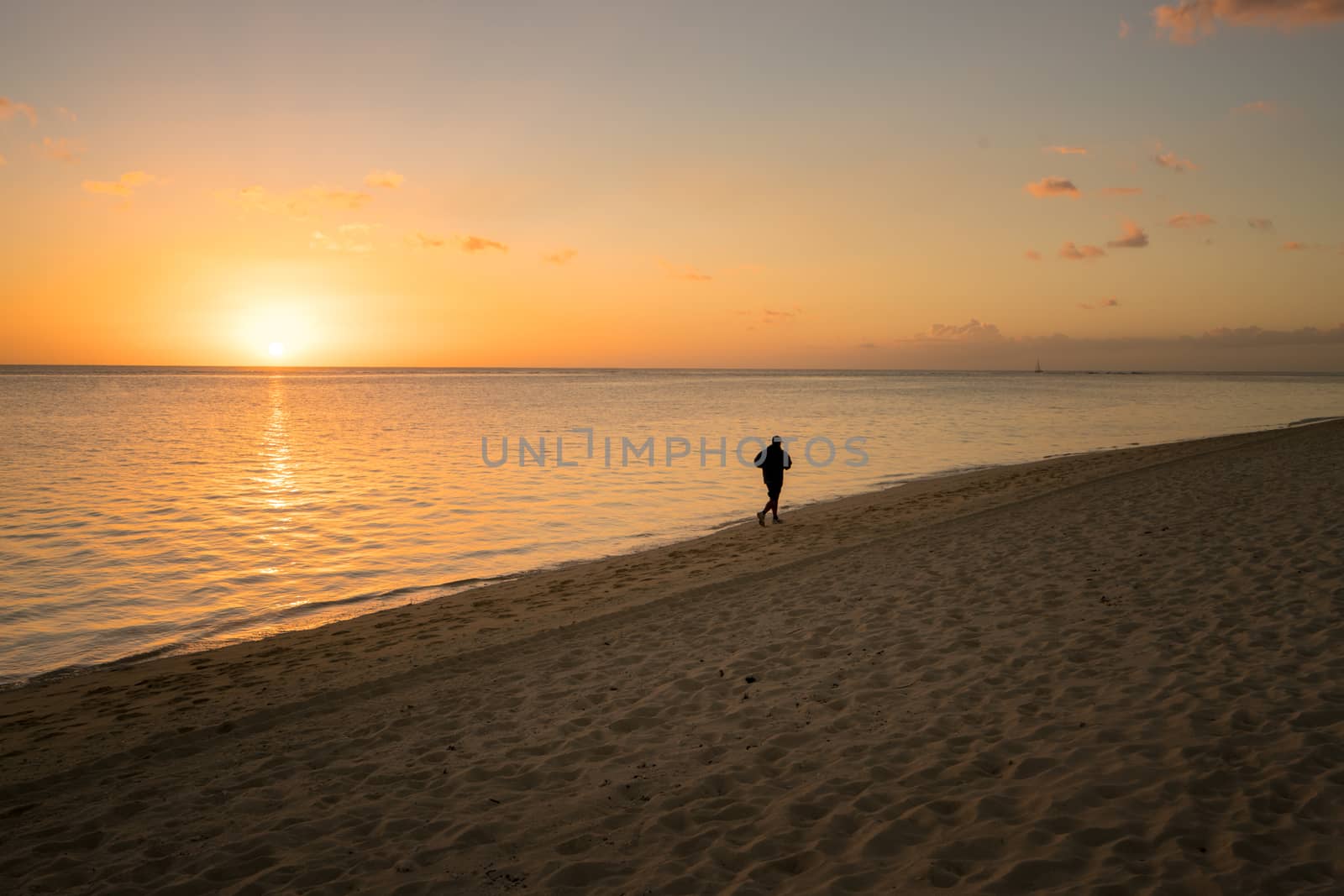 One silhouette running alone on the beach at sunset in Mauritius.