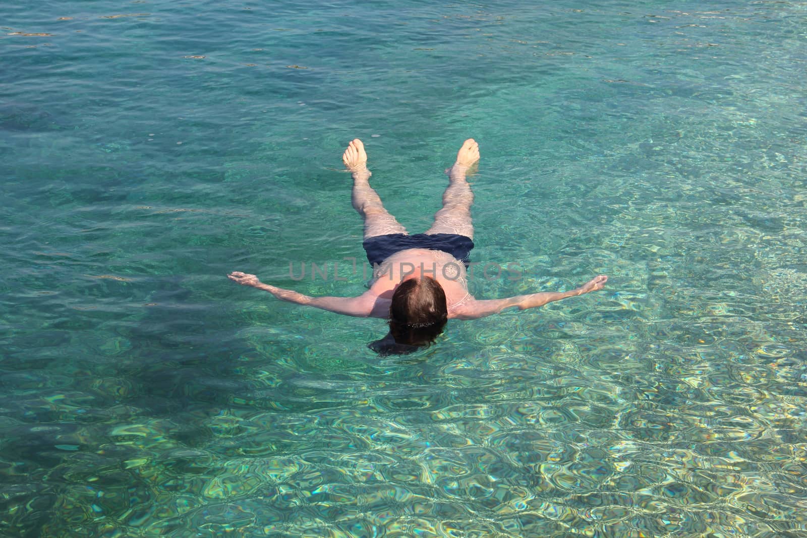 Vacation and relaxation concept, man floating relaxed on back in transparent pure blue sea water