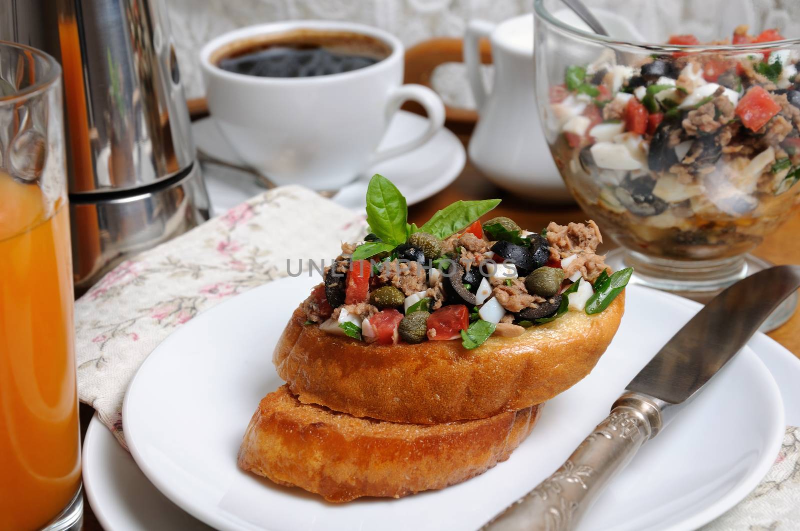 Breakfast from fried toast with chopped tuna with egg, cubes of tomatoes and olive slices, capers with a cup of coffee, a coffee pot on a tray