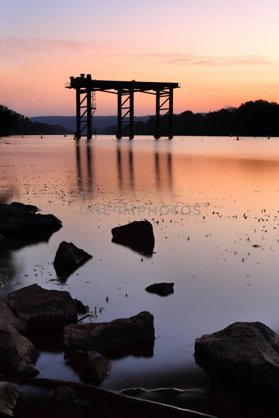 Steel construction rises from the waters of Nepean River Penrith as the sun sets casting its reflection in the waters.