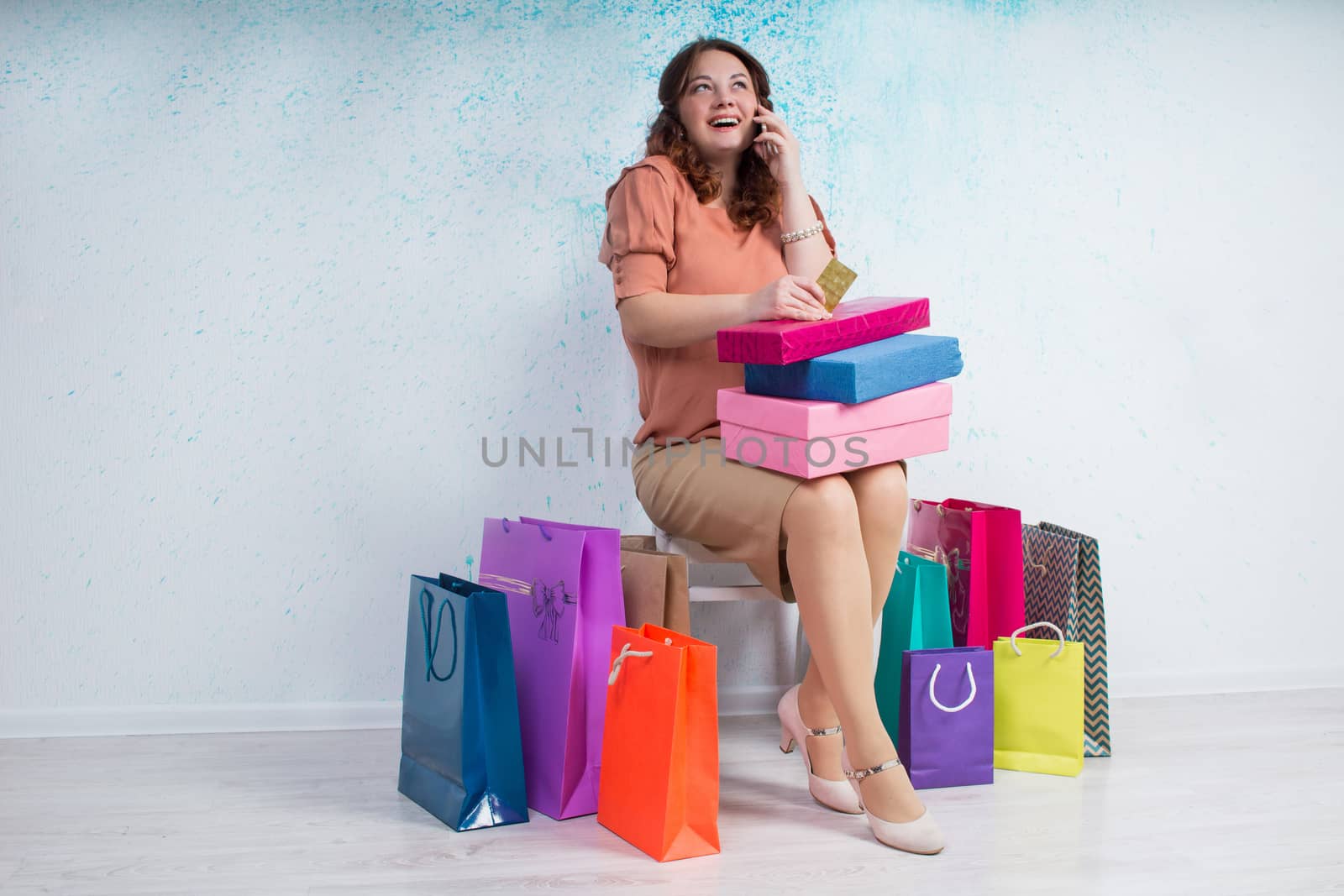 Happy smiling woman after shopping sits with colourful paper bags, boxes and banking credit card talking by phone